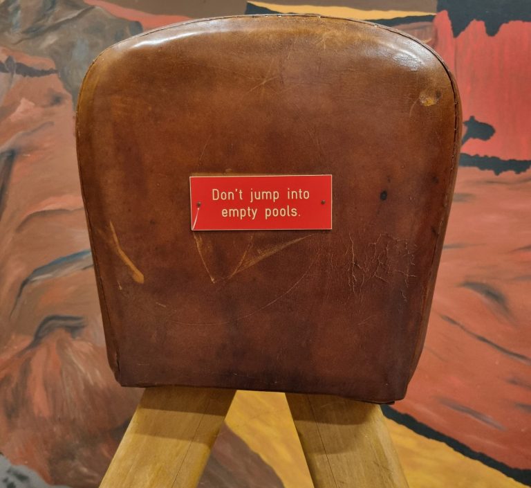 Un tabouret en cuir avec un panneau rouge indiquant "Don't you tip empty pails".