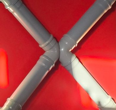 Deux coudes en PVC gris formant un "X" sur un fond vert.